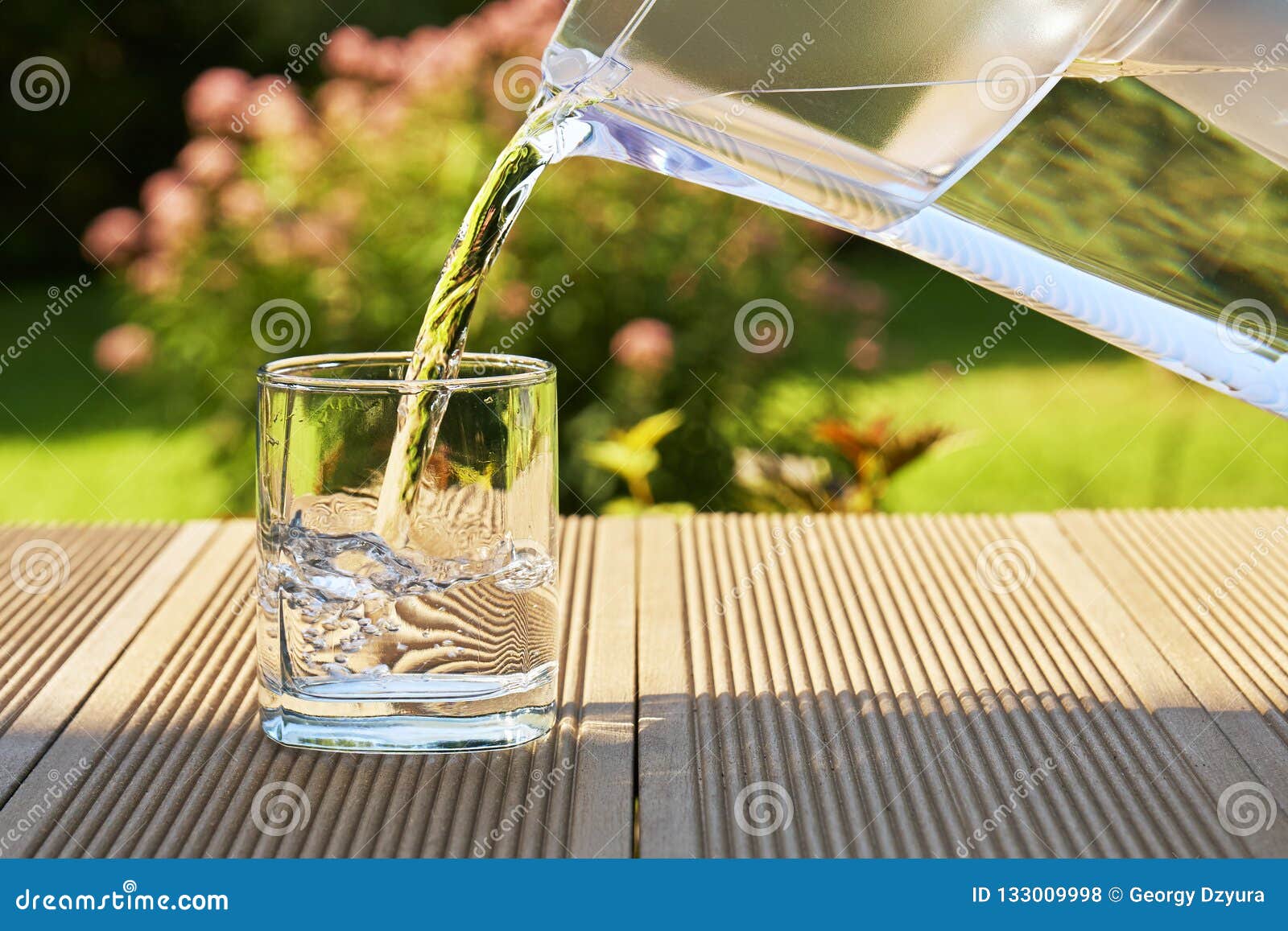 pouring clear filtered water from a water filtration jug into a glass in green summer garden in a sunny summer day