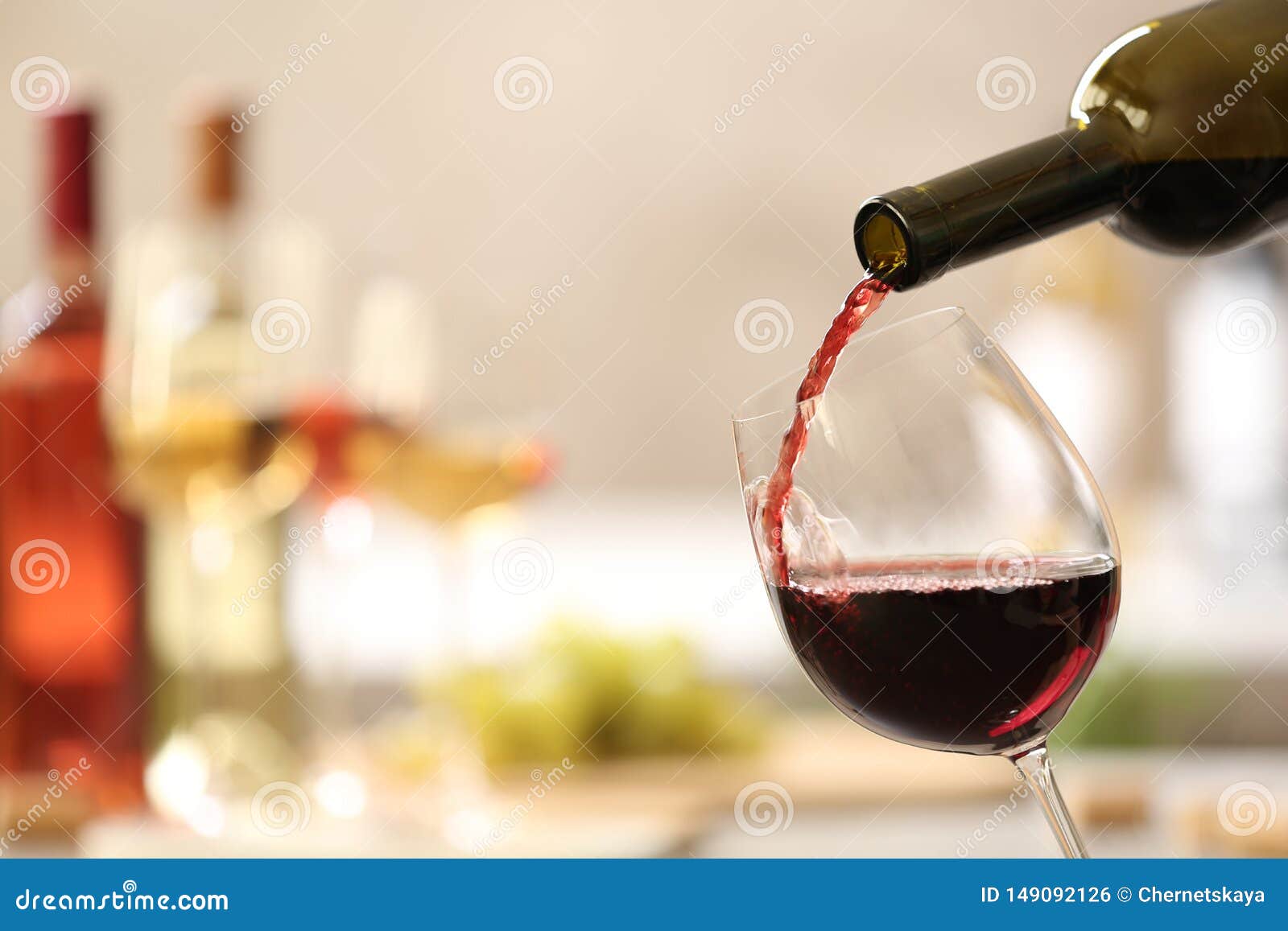 pouring red wine from bottle into glass on blurred background