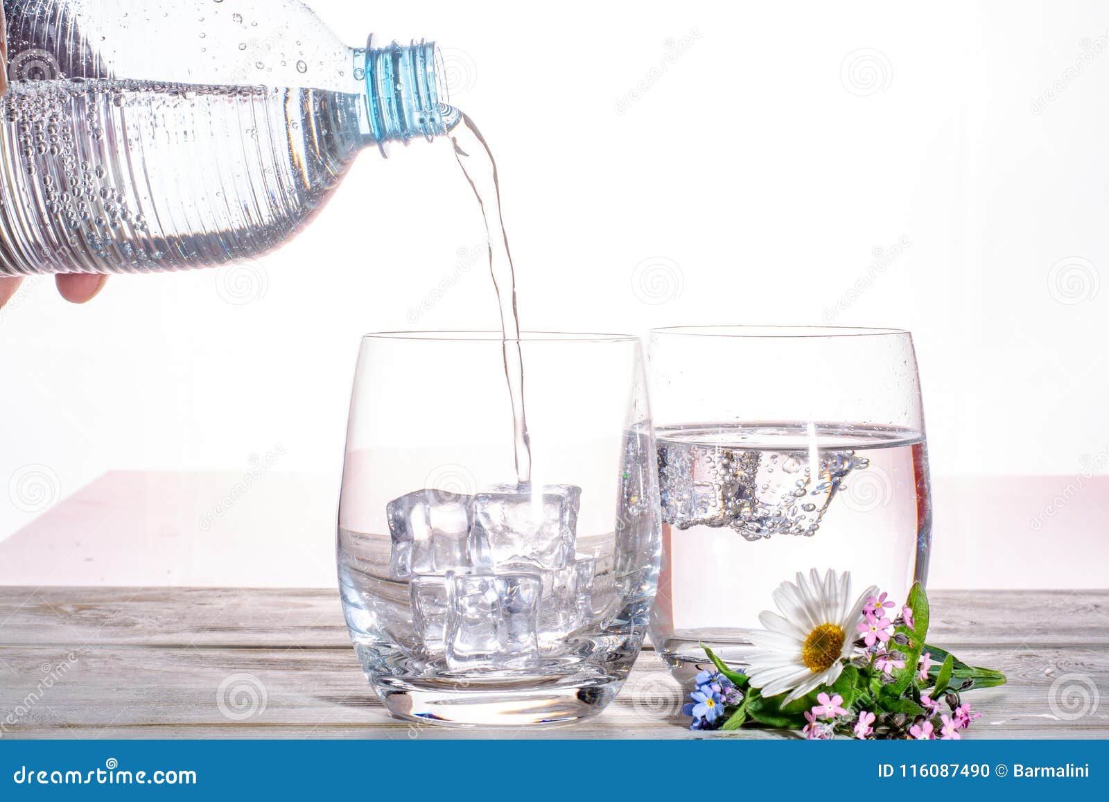 pouring of sparkling soda mineral drink water in glasses with ice cubes close up copy space