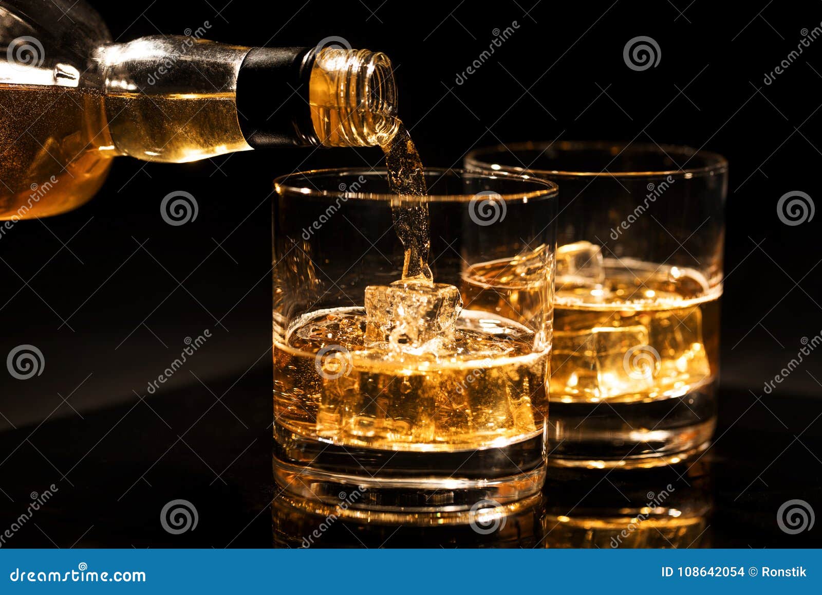 pouring whiskey into a glass from bottle with ice cubes on black