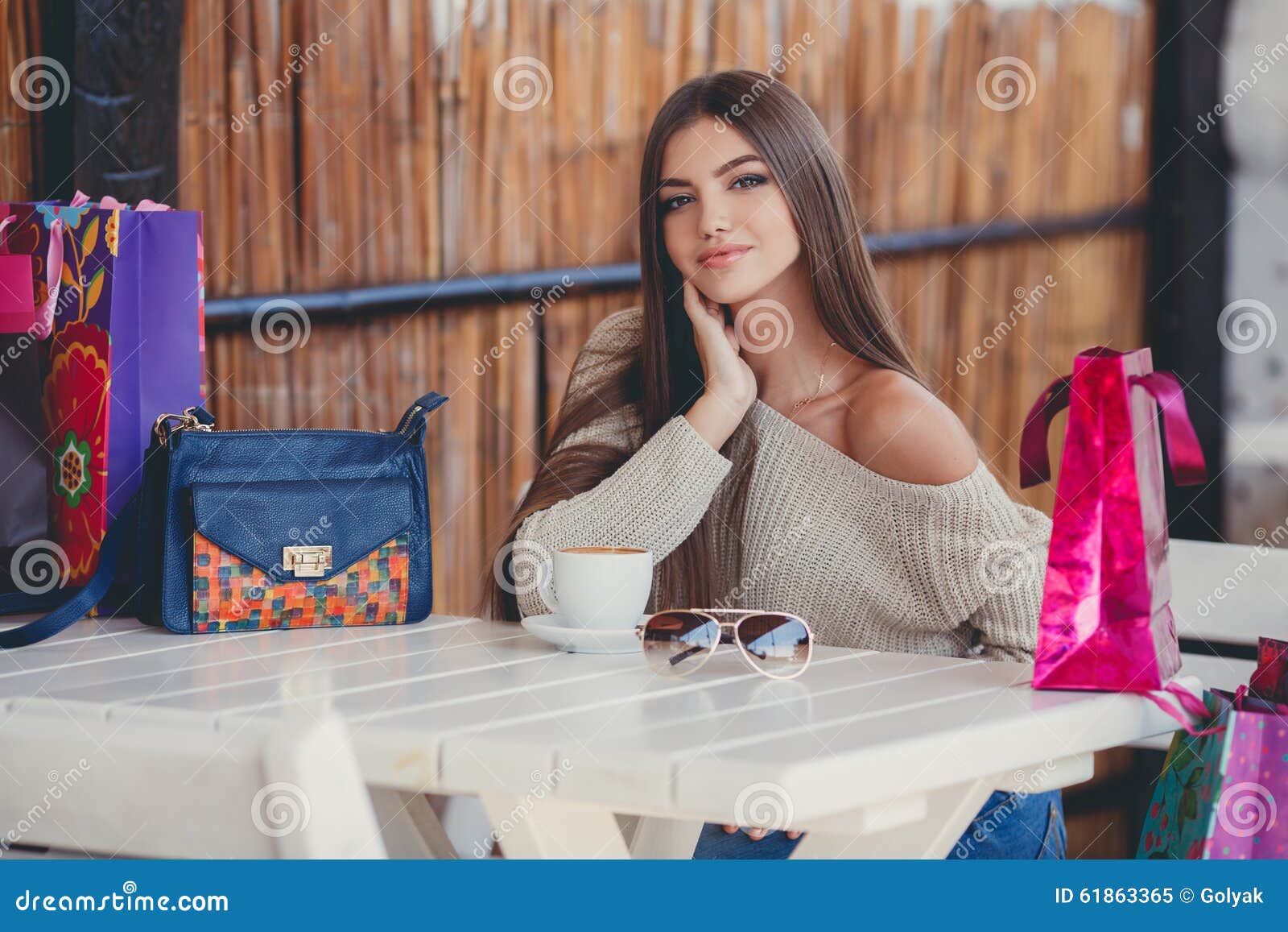 Powabna kobieta w kawiarni dla filiżanki kawy. Młoda piękna brunetki kobieta z długimi prostego włosy i brązu oczami, po tym jak znojny zakupy z barwionymi torbami, wydaje jego czasu obsiadanie przy stołem w lato kawiarni z filiżanką gorąca kawa
