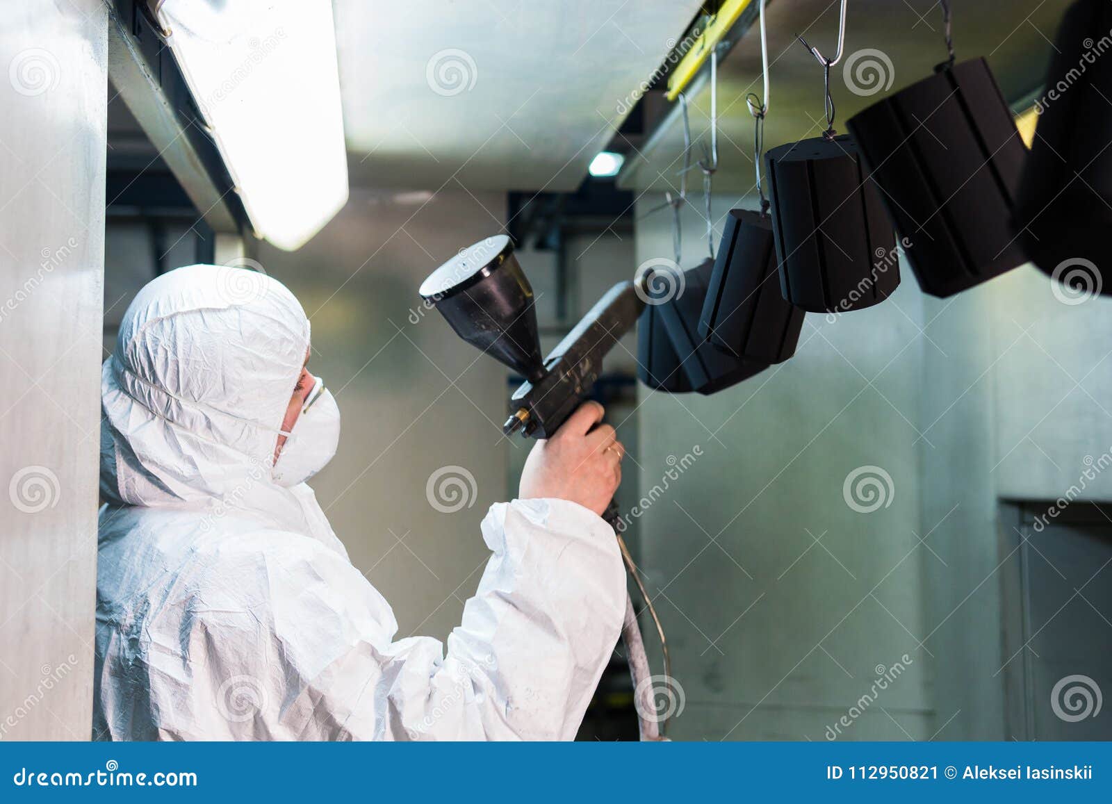 powder coating of metal parts. a man in a protective suit sprays powder paint from a gun on metal products