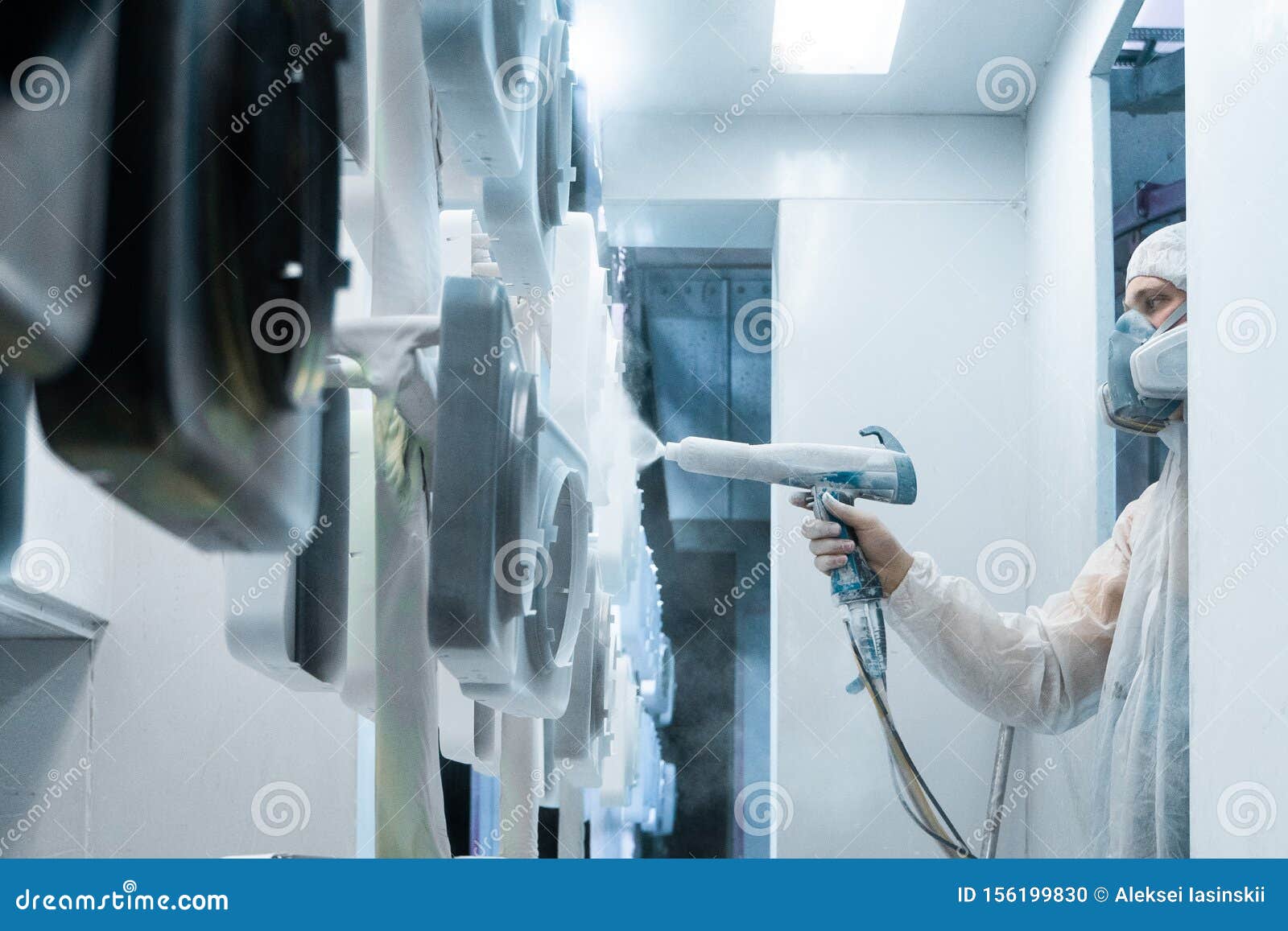 powder coating of metal parts. man in a protective suit sprays white powder paint from a gun on metal products