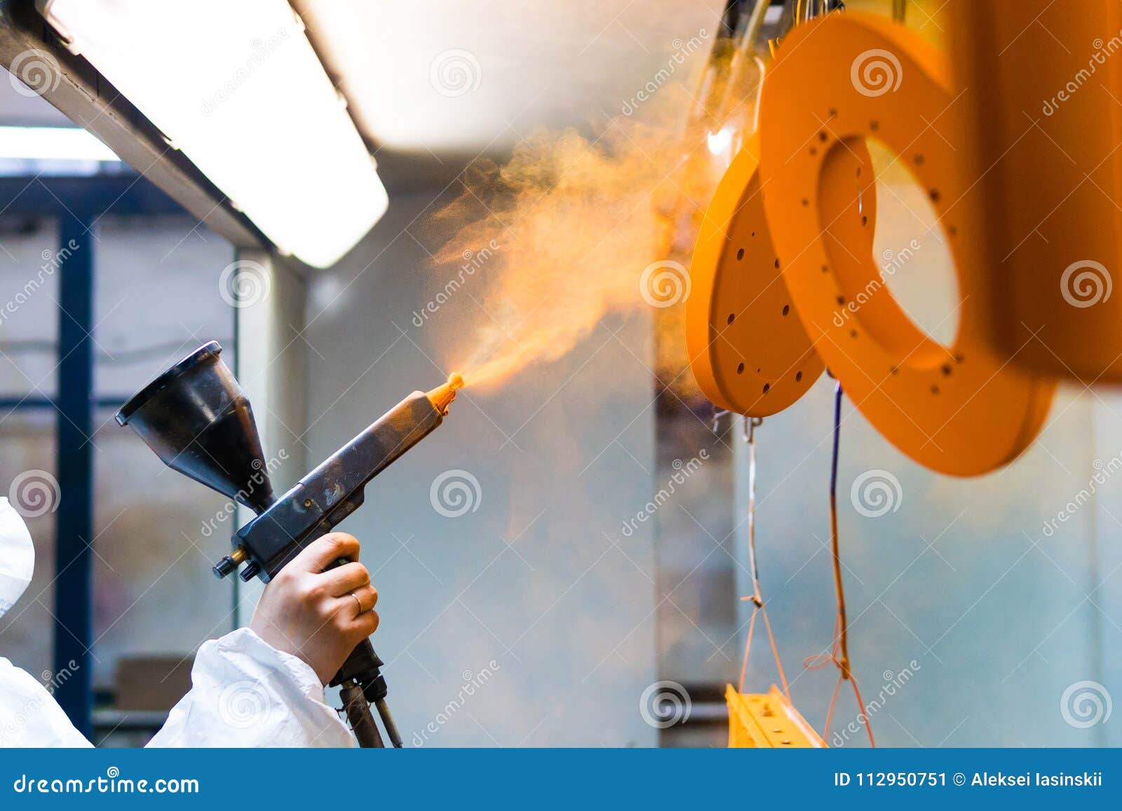 powder coating of metal parts. a woman in a protective suit sprays powder paint from a gun on metal products