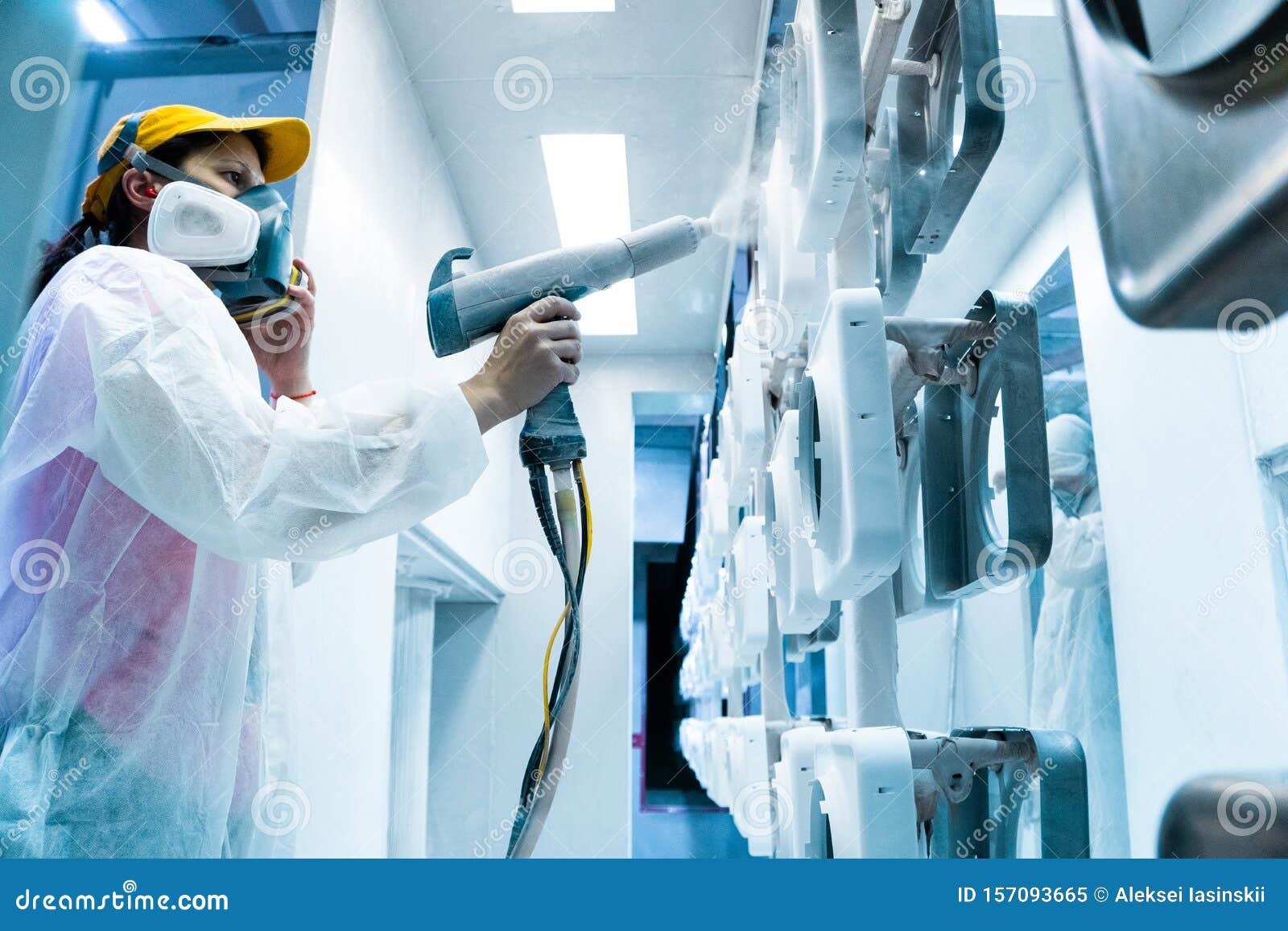 powder coating of metal parts. a woman in a protective suit sprays white powder paint from a gun on metal products