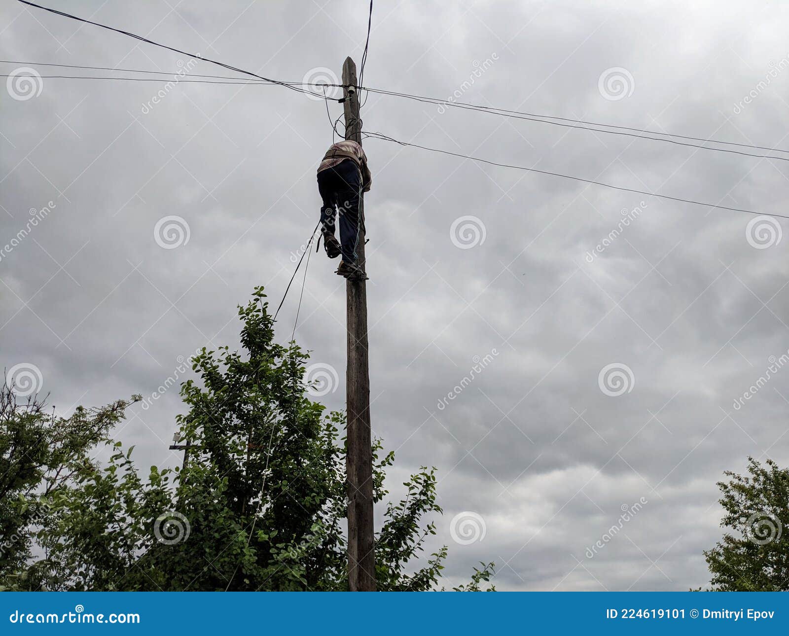 Power Electrician Lineman at Work on Pole Against the Gloomy Sky Stock