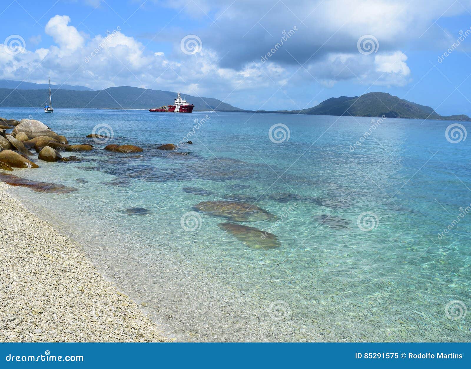 Praia da ilha de Fitzroy em Queensland. Esta foto mostra uma praia da ilha de Fitzroy com águas muito claras, um barco e alguns mounatins no fundo