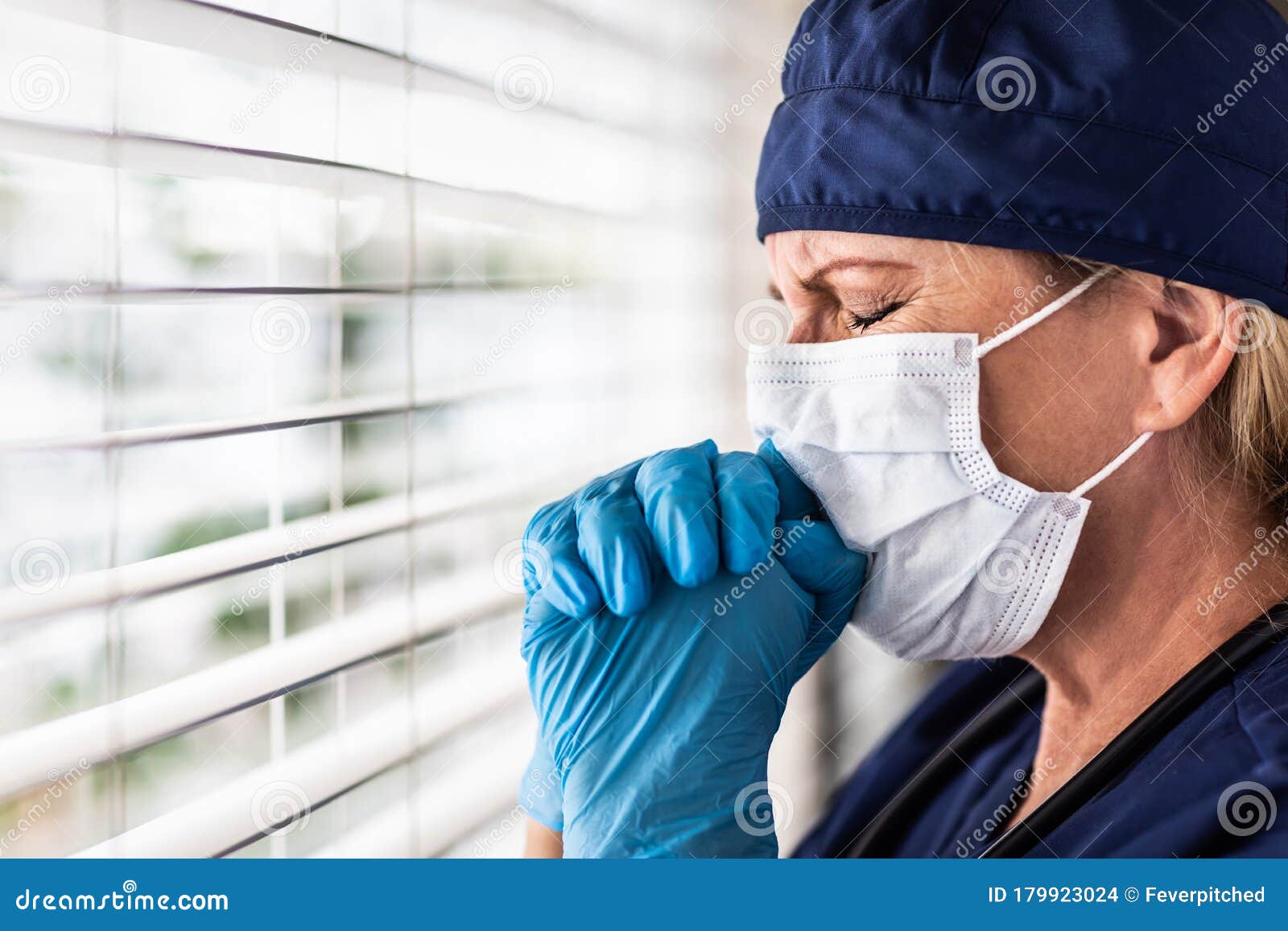 prayerful stressed female doctor or nurse on break at window wearing medical face mask