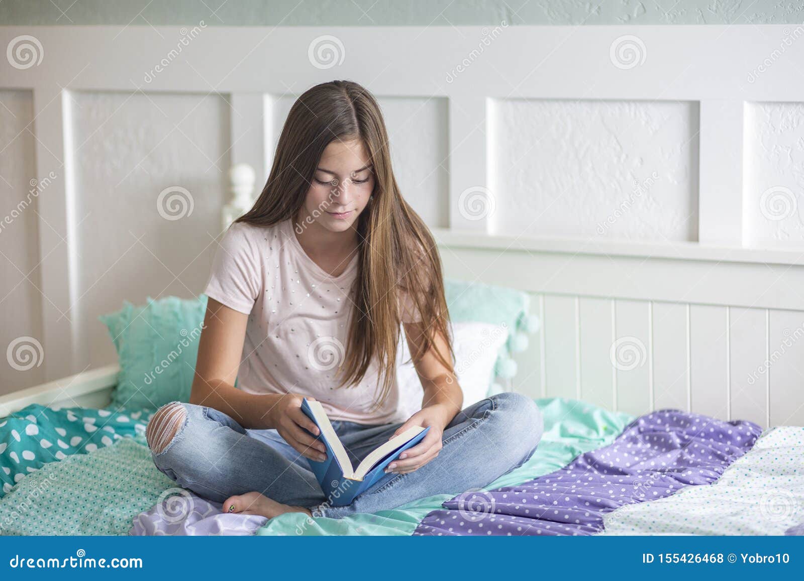 pre-adolescent teen girl reading a book lying in bed at home. candid indoor photo with focus on the foreground and copy space