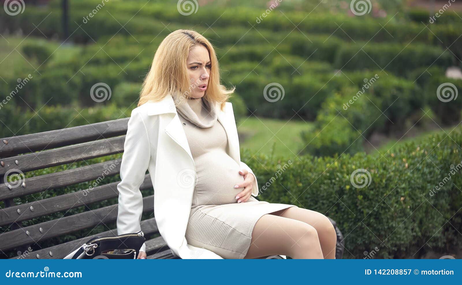pregnant blond woman hardly breathing, sitting on bench, feeling abdominal pain