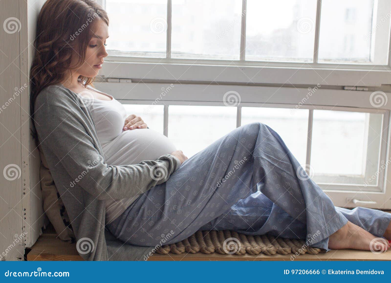 Pregnant female is sitting on the windowsill. Pregnant brunette female sitting on the windowsill .