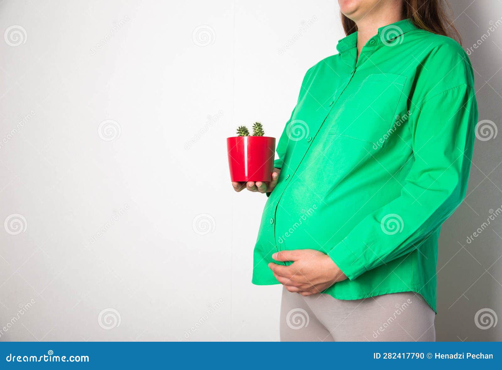 a pregnant girl in a green blouse holds a red cactus pot. coznept of cutting pains and colic in the abdomen in pregnant