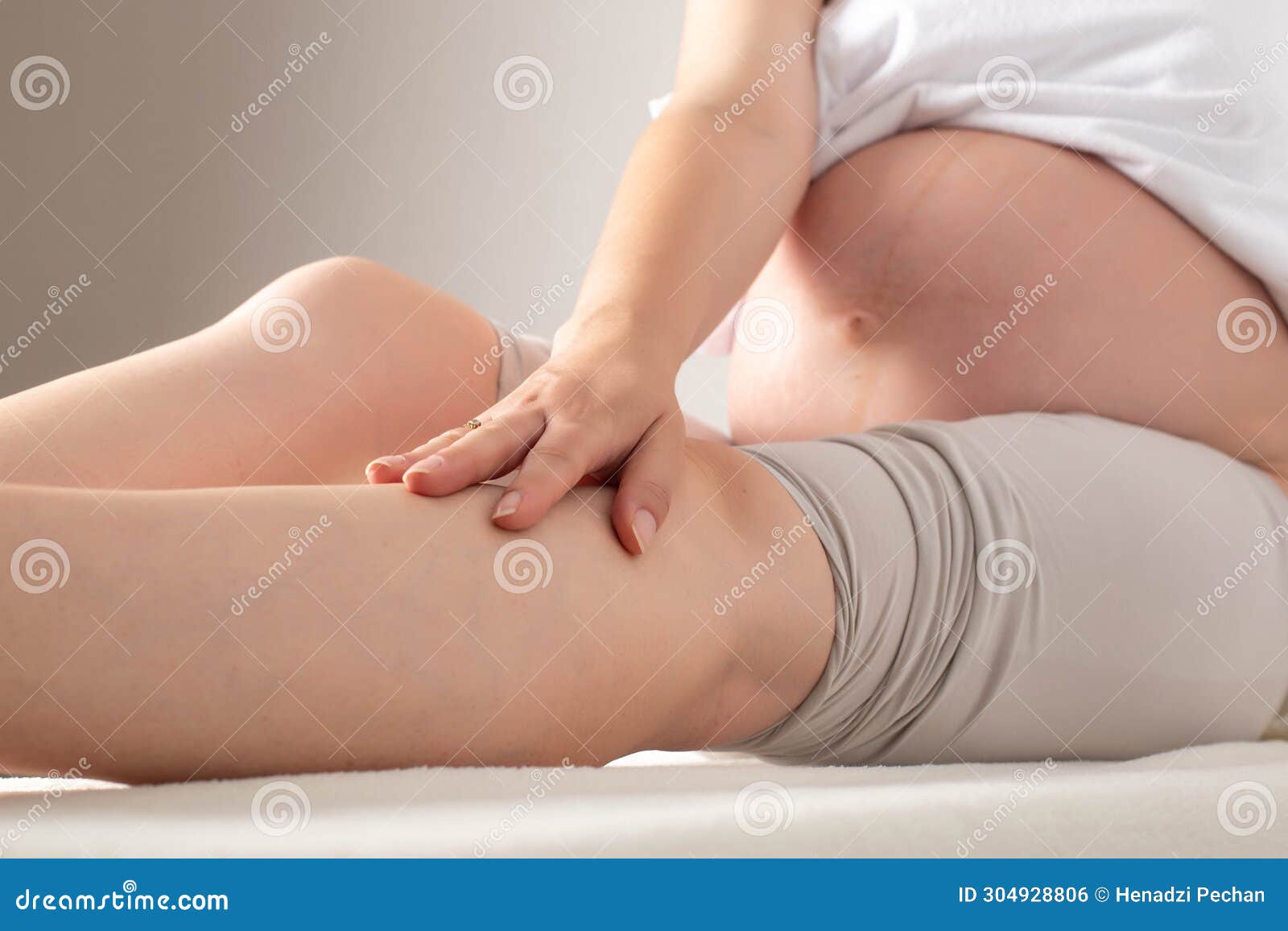 pregnant girl sits and holds her leg on a white background. concept of heaviness in the legs during pregnancy. varicose