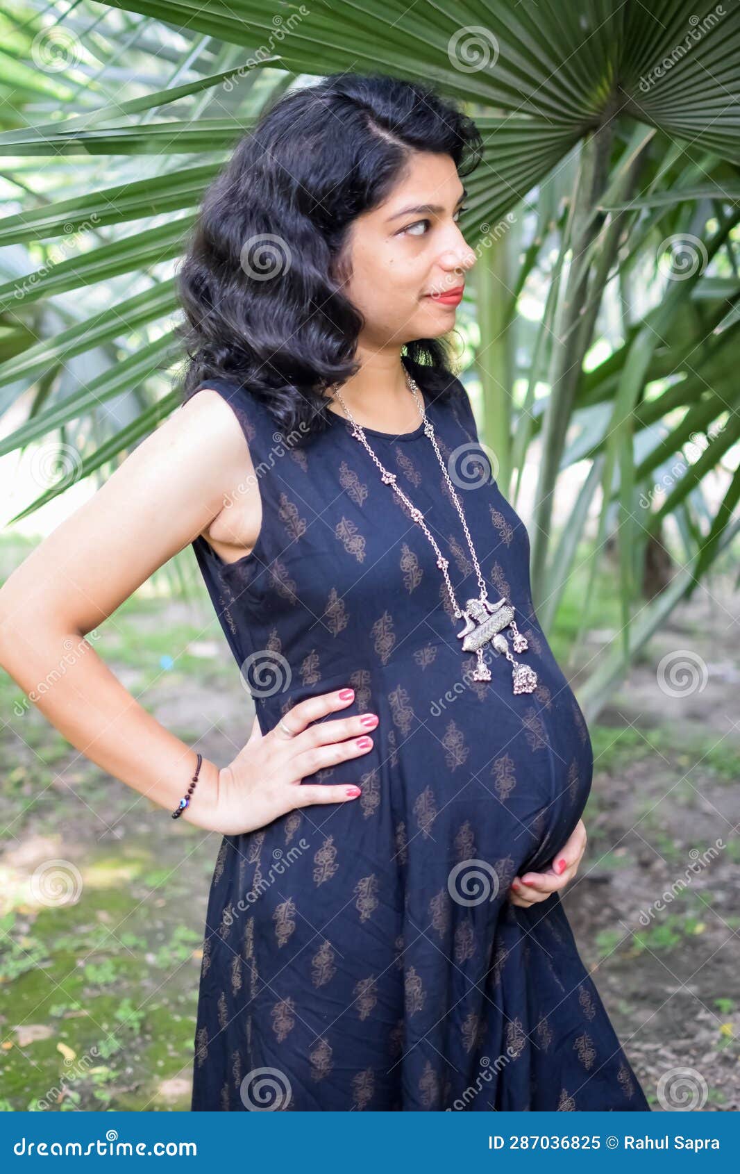 A pregnant Indian lady poses for outdoor pregnancy shoot and hands on  belly, Indian pregnant woman