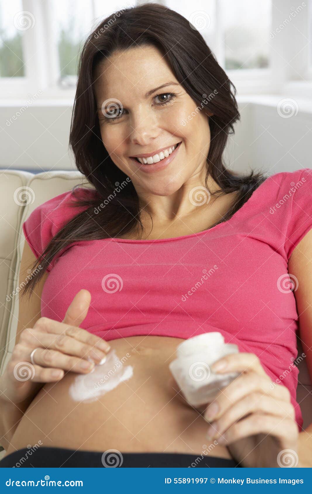 pregnant woman applying moisturiser to belly at home