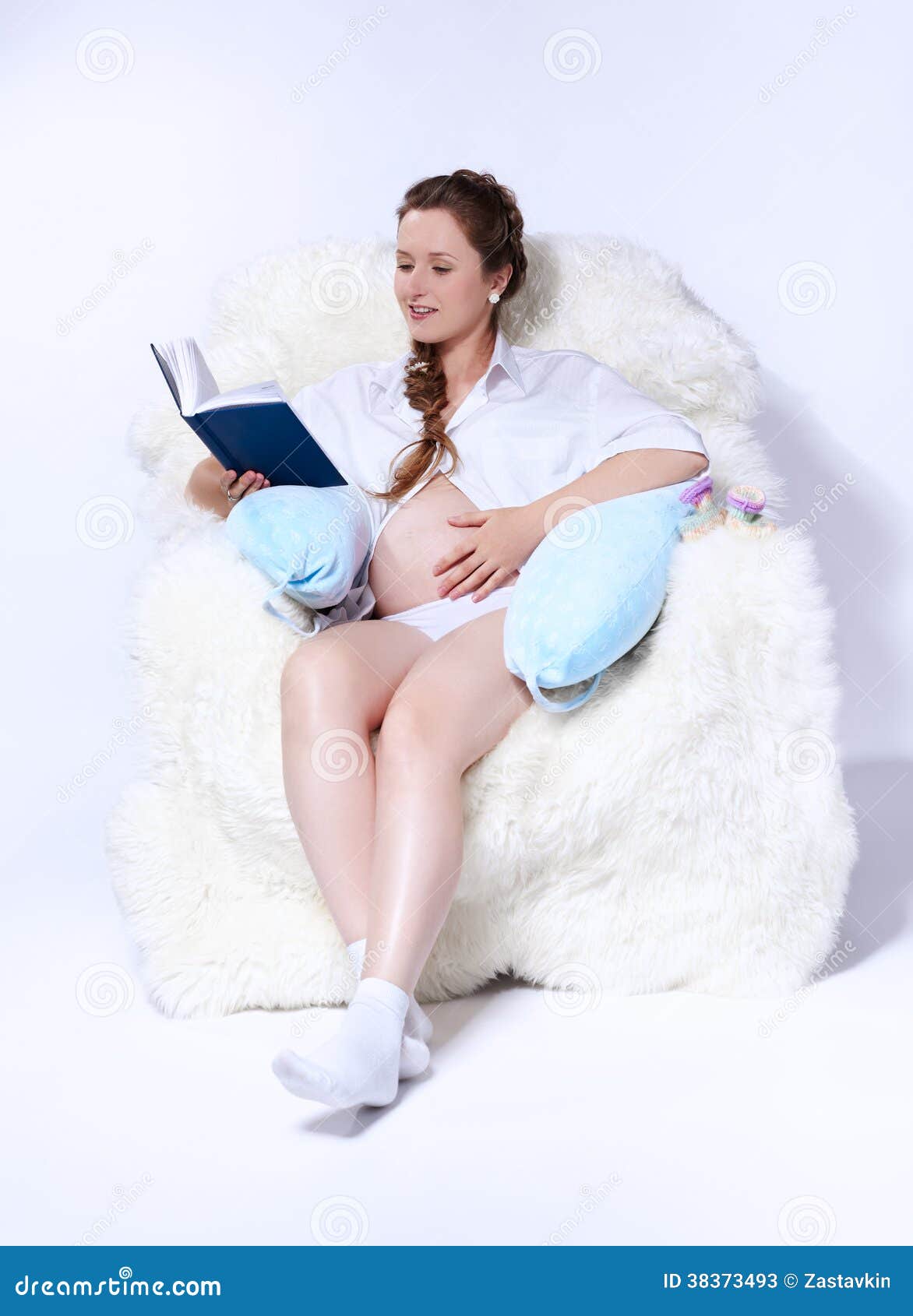 Pregnant woman in arm-chair. Portrait of young beautiful pregnant woman in white furry arm-chair and reading book