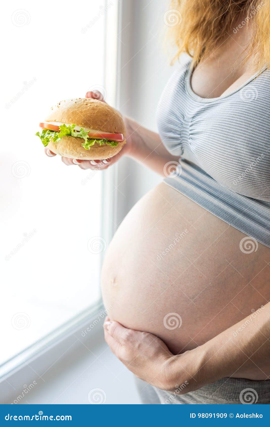 A Pregnant Woman With Belly By The Window Holding A Burger ... A Pregnant Woman With Belly By The Window Holding A Burger ...