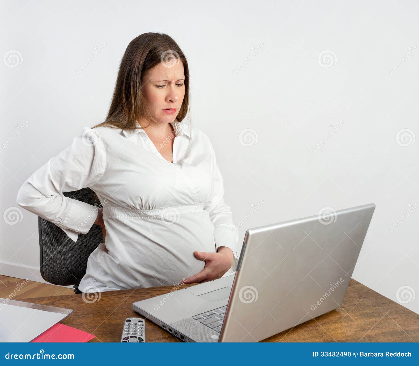 Pregnant young woman at a desk at laptop computer feeling first labor 