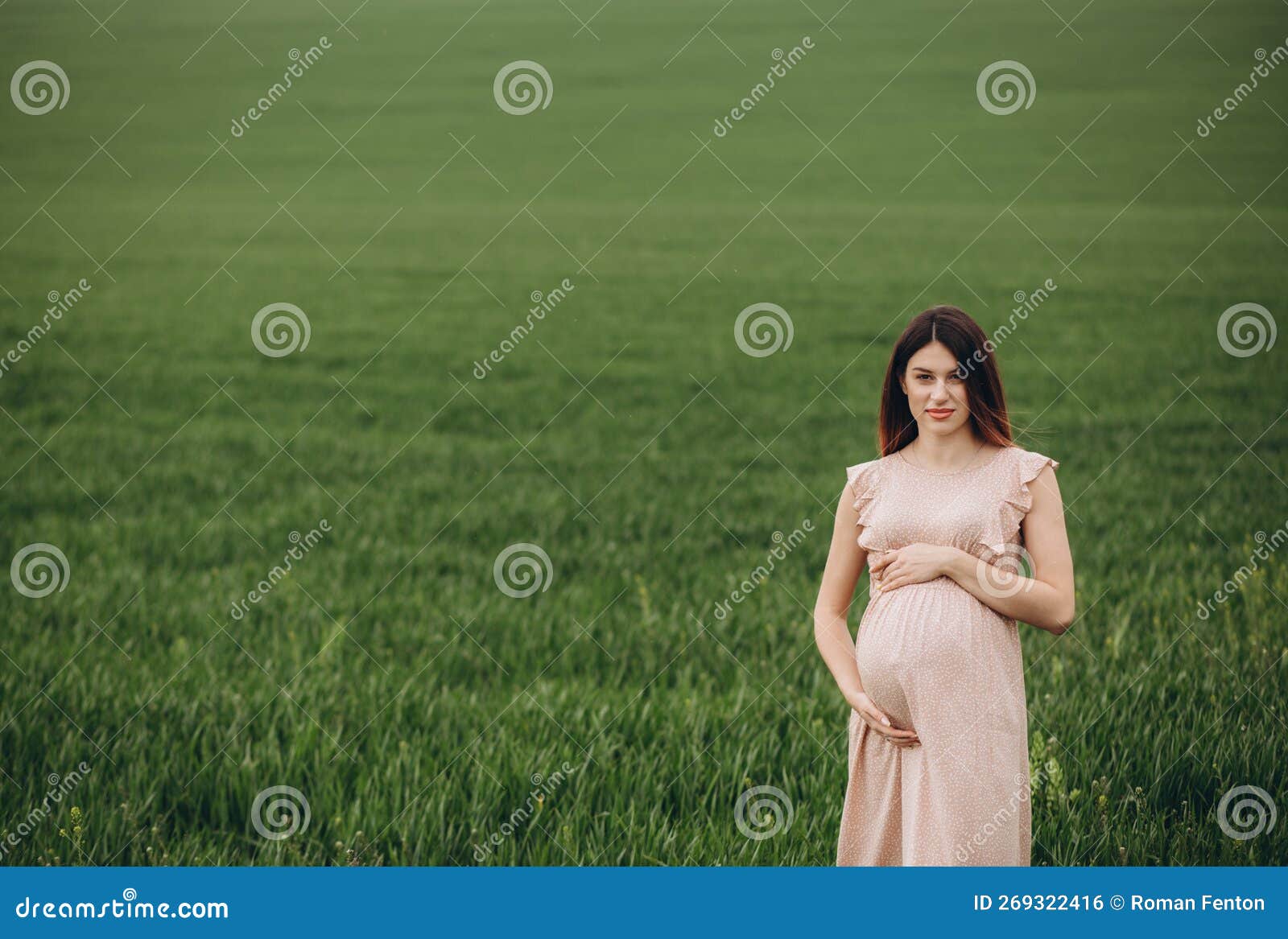 Pregnant Woman Stand at the Field with Green Grass and Embrace Her ...