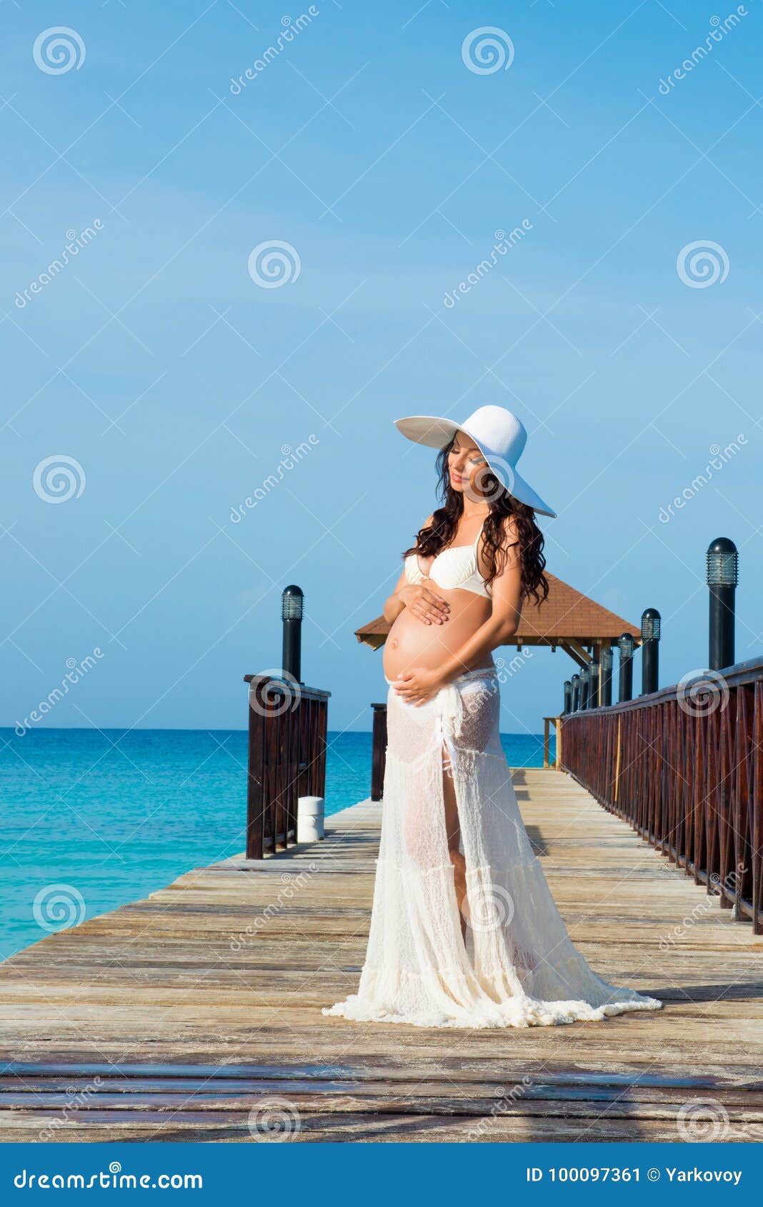 Pregnant Woman Is Standing On A Wooden Pier Hugging Her Stomach Against The Sea Dominican 