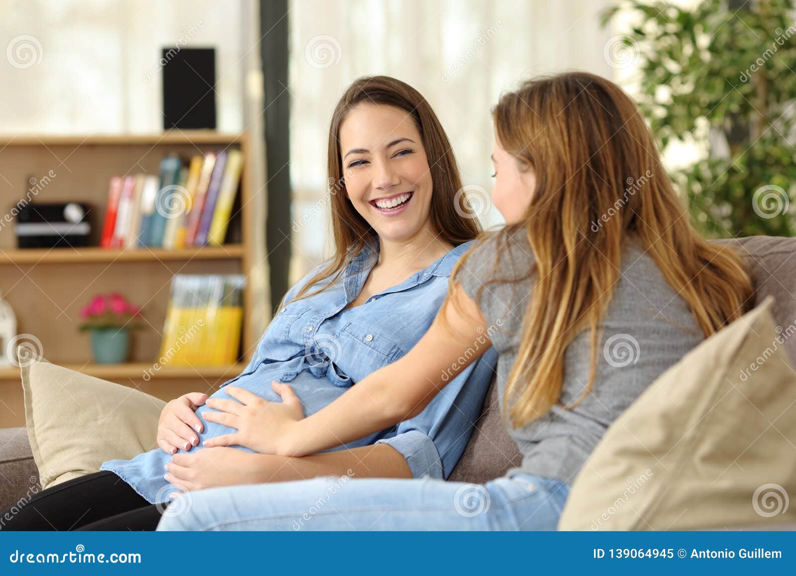 pregnant woman talking with a friend who touches her belly