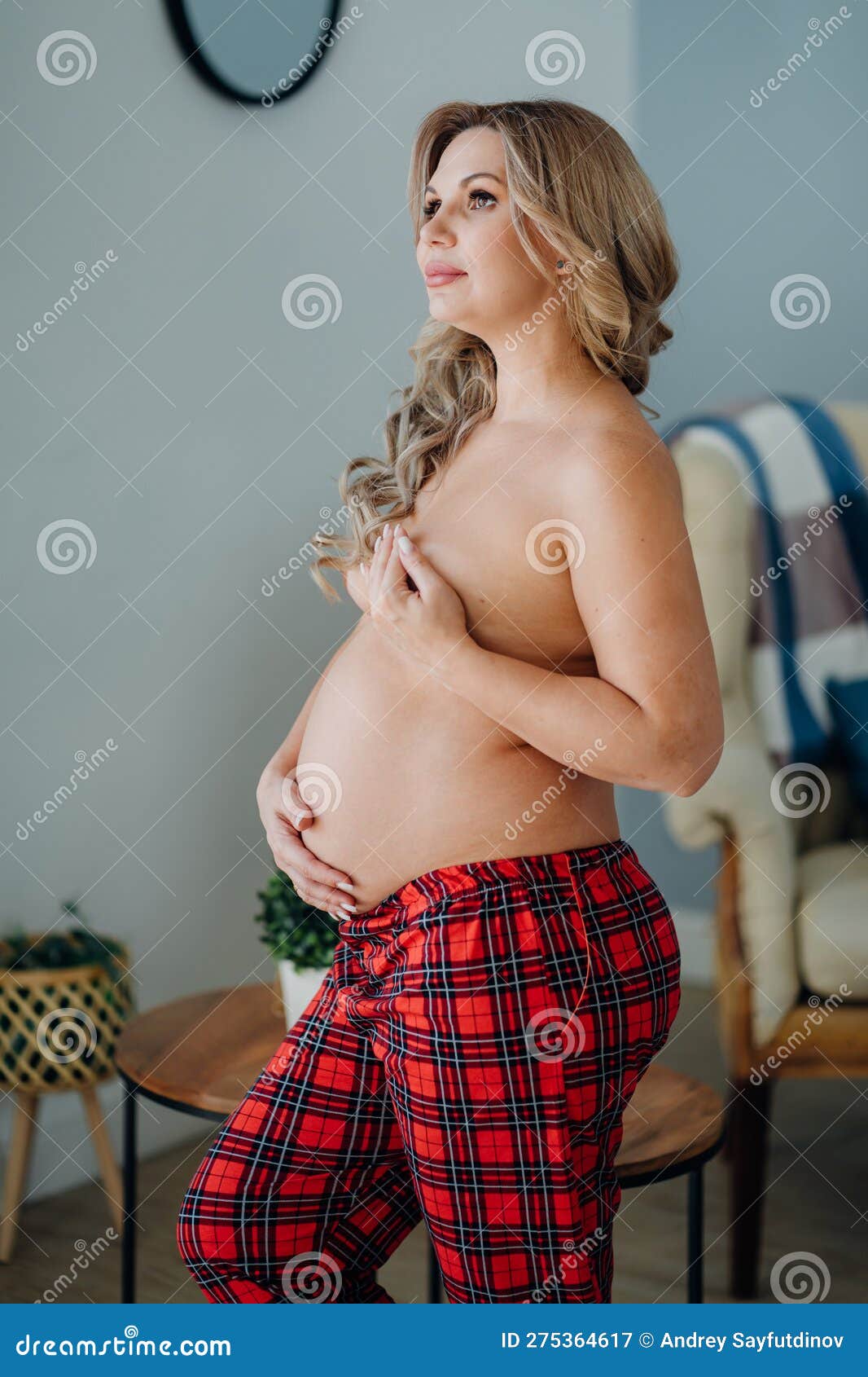 A Pregnant Woman Topless in Pajama Pants in Profile in a Home