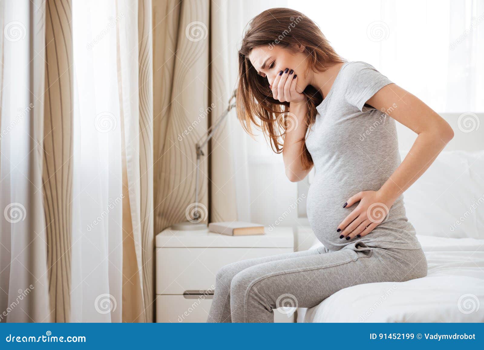 pregnant young woman sitting on bed and feeling sick