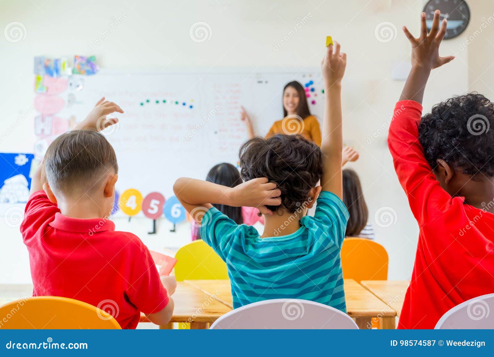 preschool kid raise arm up to answer teacher question on whiteboard in classroom,kindergarten education concept