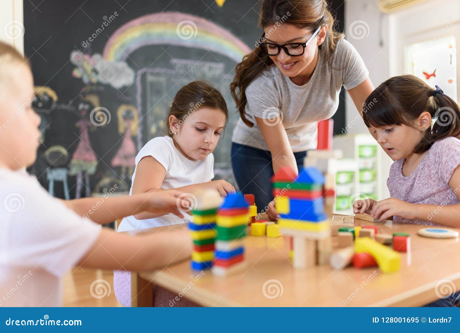 preschool teacher with children playing with colorful wooden didactic toys at kindergarten