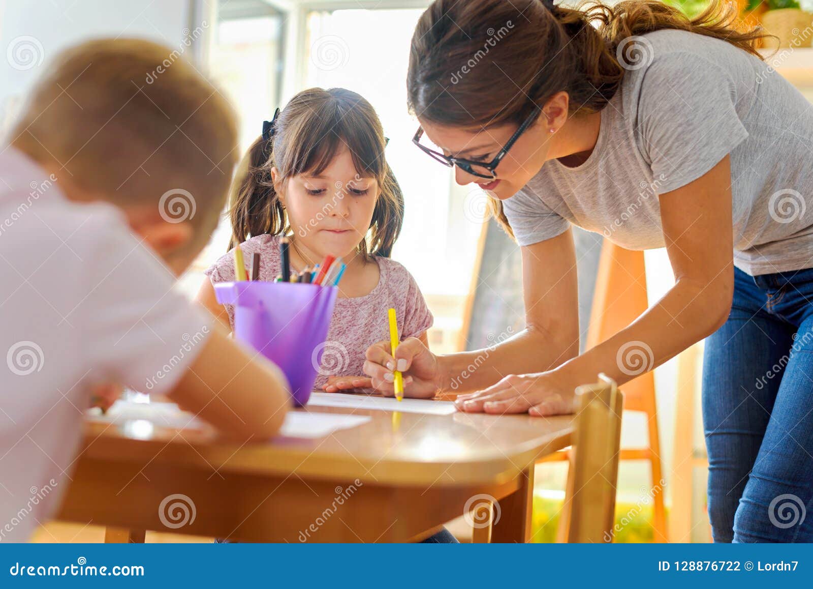 preschool teacher looking at smart child learning to write and draw