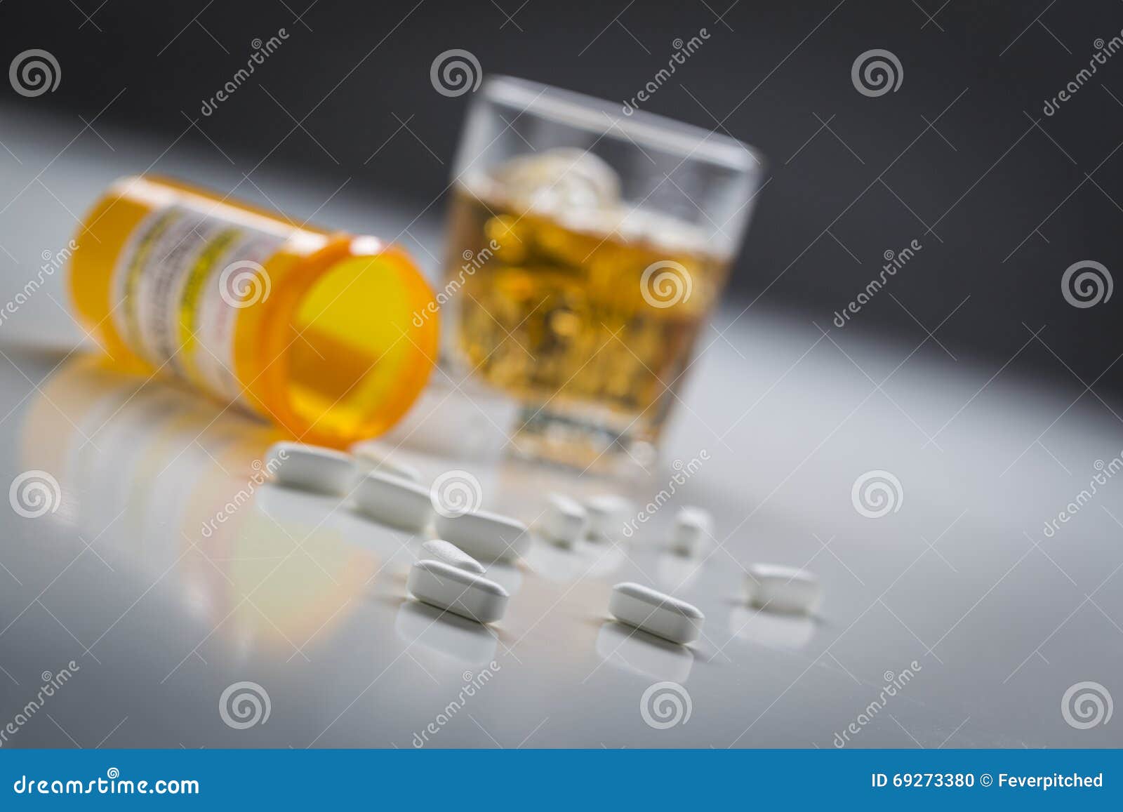 prescription drugs spilled from fallen bottle near glass of alcohol
