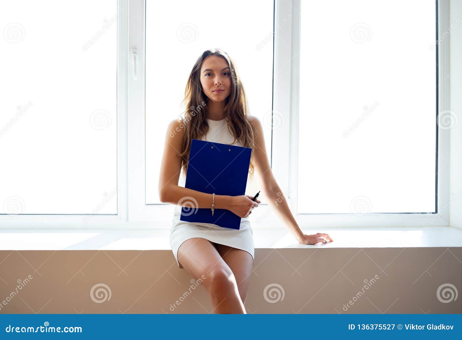 pretty business woman with clipboard sitting on window sill in the office
