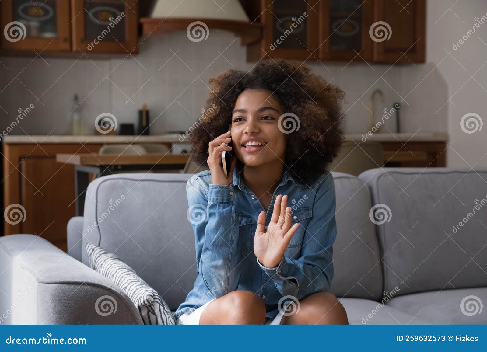 pretty african teenage girl sits on sofa blab on cellphone