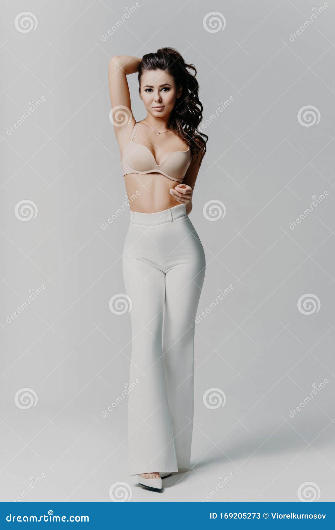 Pretty Dark Haired Young Woman Wears Bra and White Trousers, Keeps Hand  Behind Head, Has Perfect Body, Stands in Full Length Stock Image - Image of  model, body: 169205273