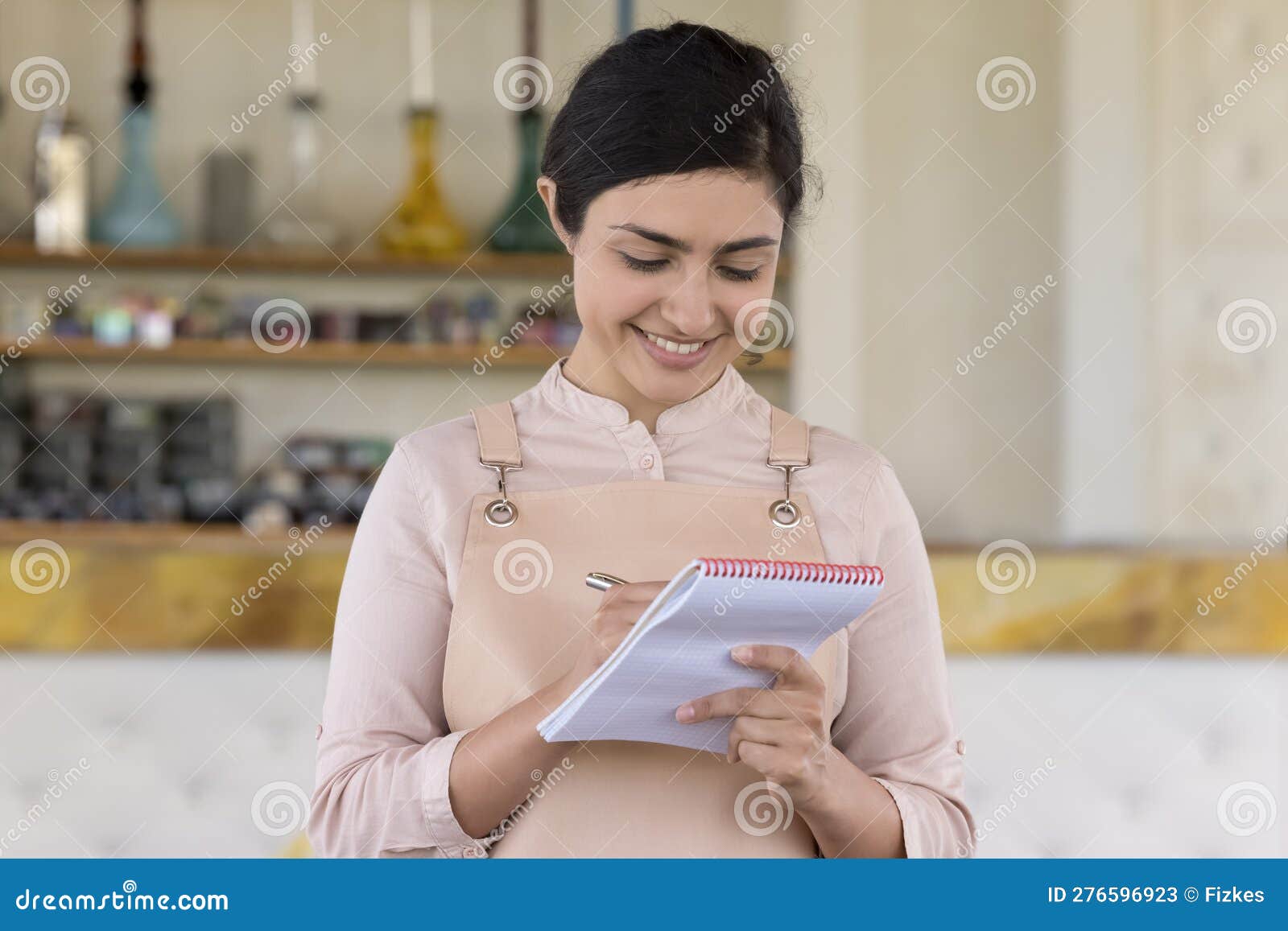 Pretty Indian Waitress Writing in Notepad Standing at Workplace Stock