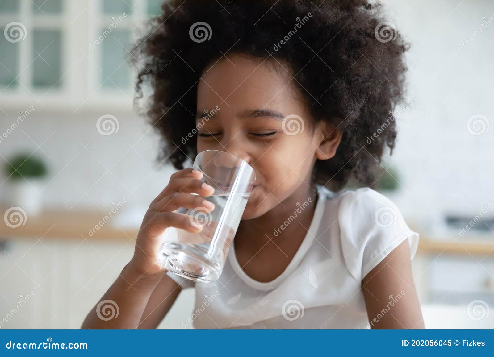 pretty little african american girl drinking fresh water in kitchen