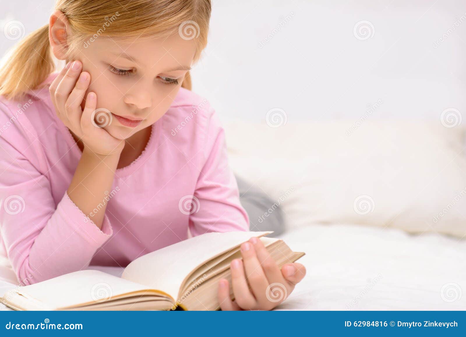 Pretty little girl reading. Interesting novel. Nice glad little girl holding book and reading it while lying on the sofa