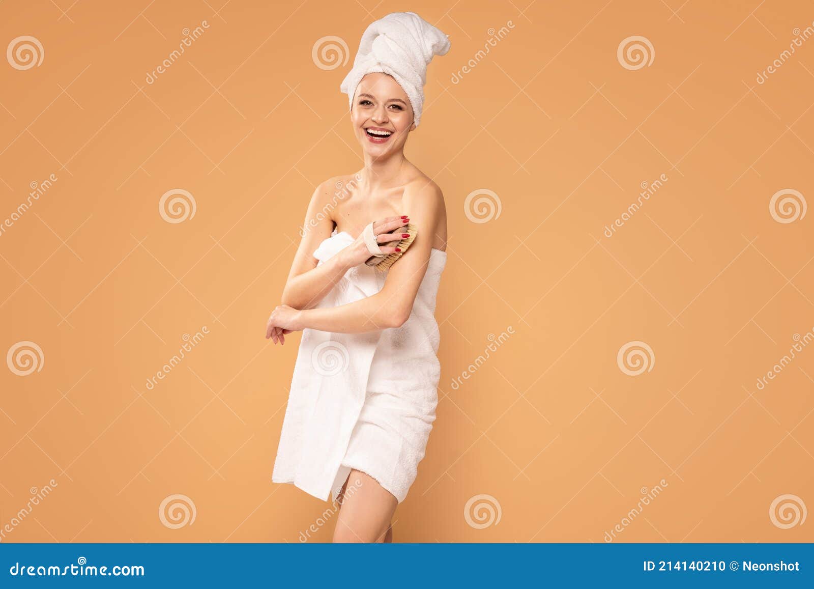 pretty smiling woman brushing her skin, cares about hygiene, wearing white towel on head