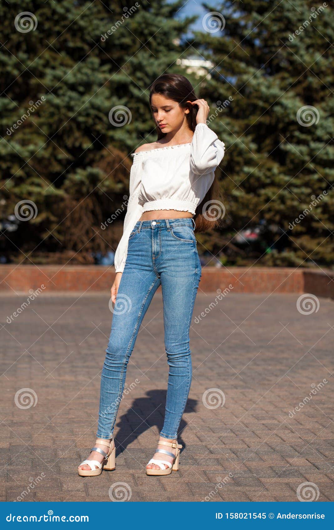 Gorgeous brunette girl with long flowing hair dressed in jeans jacket and jeans  poses standing on Stock Photo by leikapro