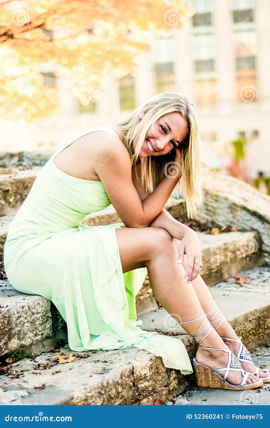 Pretty teen girl with blonde hair. Pretty beautiful young teenage girl / woman / female with blonde hair. sitting on old stone steps wearing an elegant mint green formal fashion prom dress.