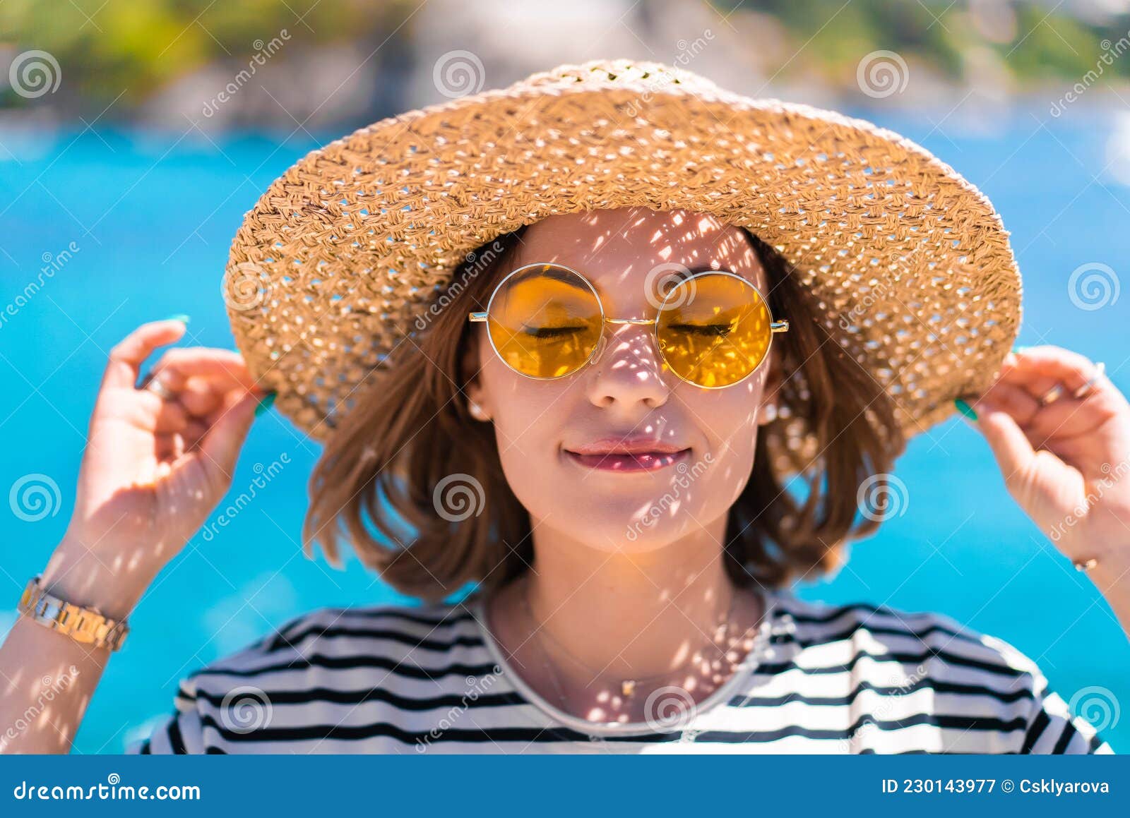 Pretty Woman In Yellow Sunglasses And Straw Hat Smiling Sincerely To Camera On Teal Blue Sea 