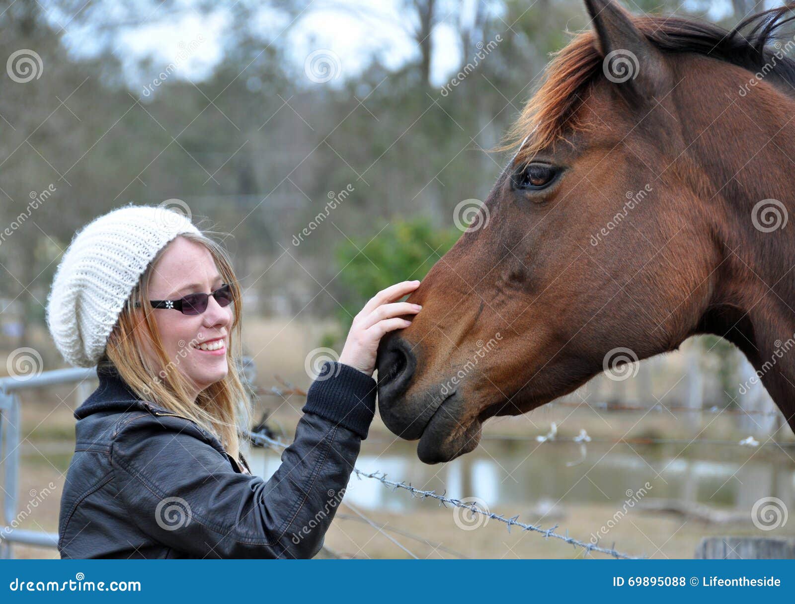 pretty young happy woman outdoors with pet horse stroking him