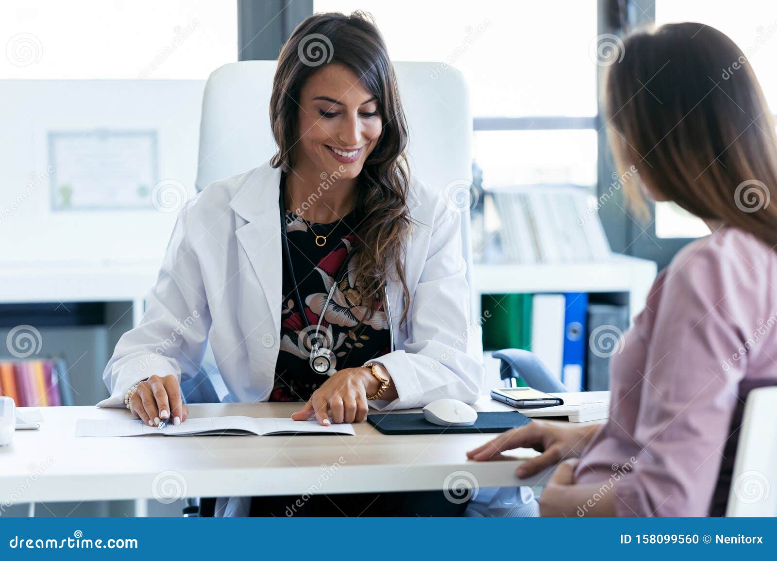 pretty young woman gynecologist reviewing the documents of her pregnant patient in the clinic
