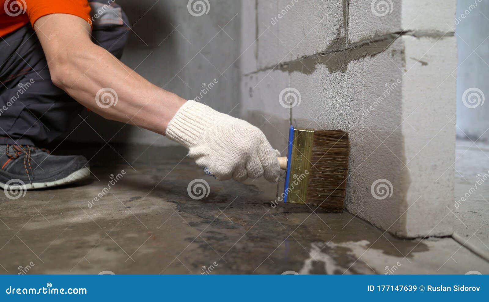 Worker Wets the Concrete Floor with a Brush. Primer Concrete Floor for