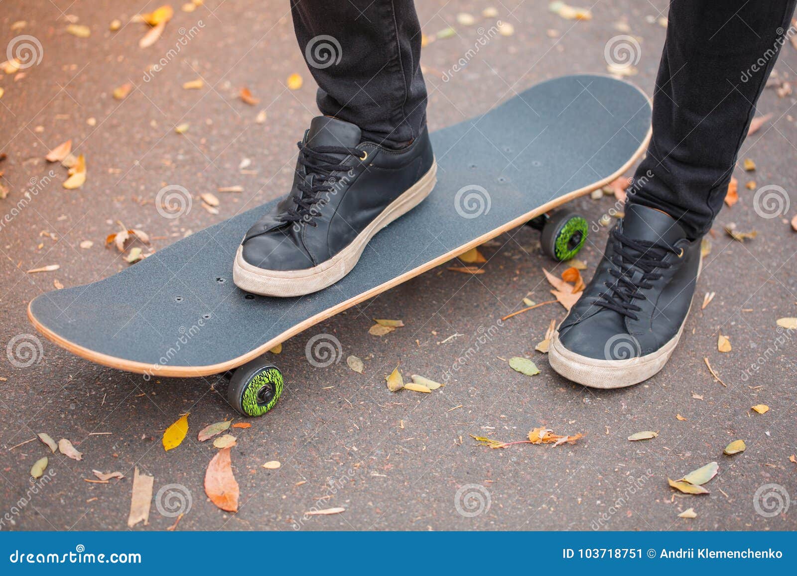 Primo piano di un piede del ` s del skateboarder in scarpe da tennis nere. Il primo piano di un piede del ` s del skateboarder nel krosovkah nero su un pattino, fra le foglie di autunno, il piede destro di un skateboarder sta su un pattino Il concetto dello sport