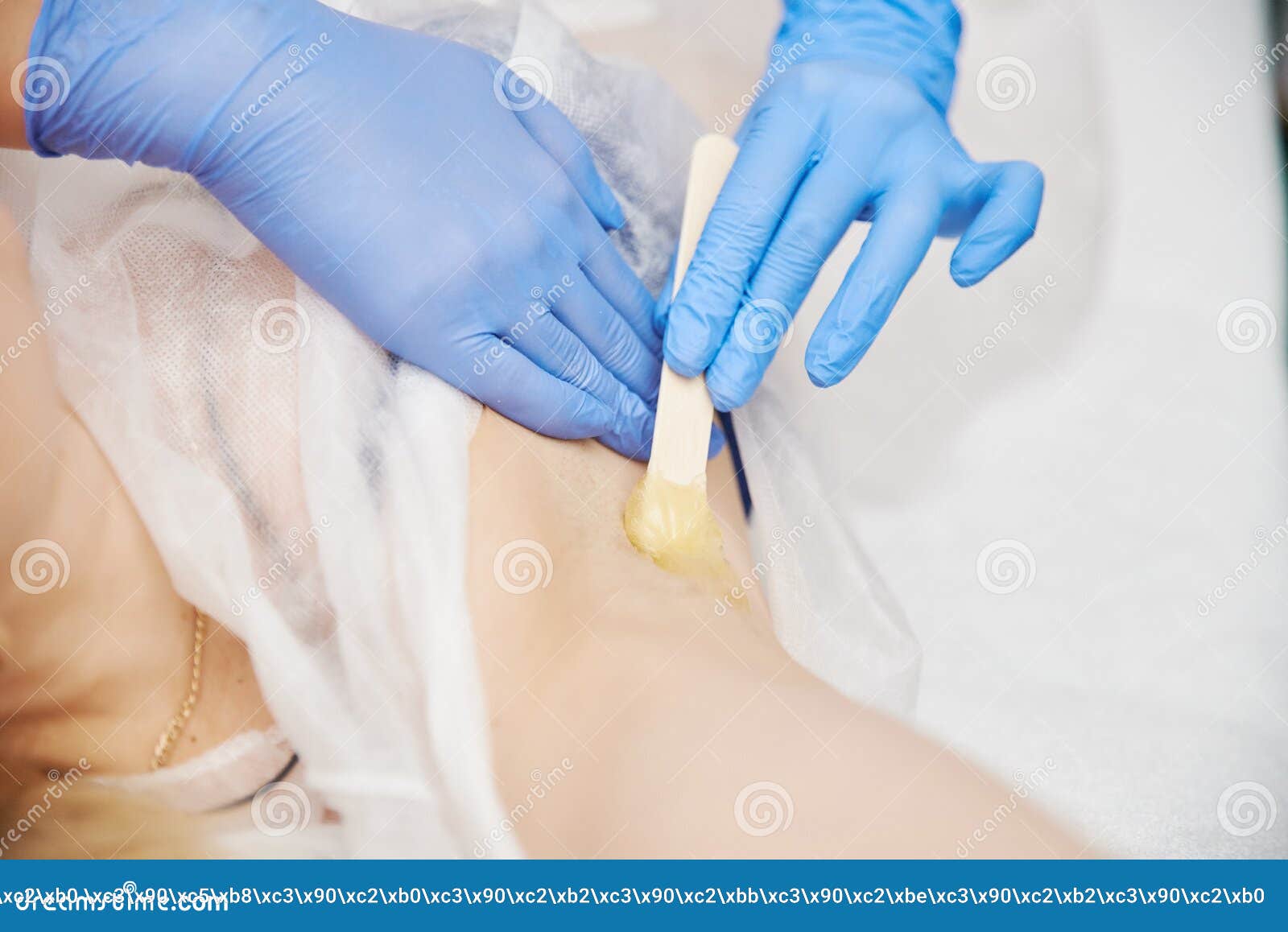 the procedure shugaring. master in blue medical gloves apply sugar paste to the client`s armpit