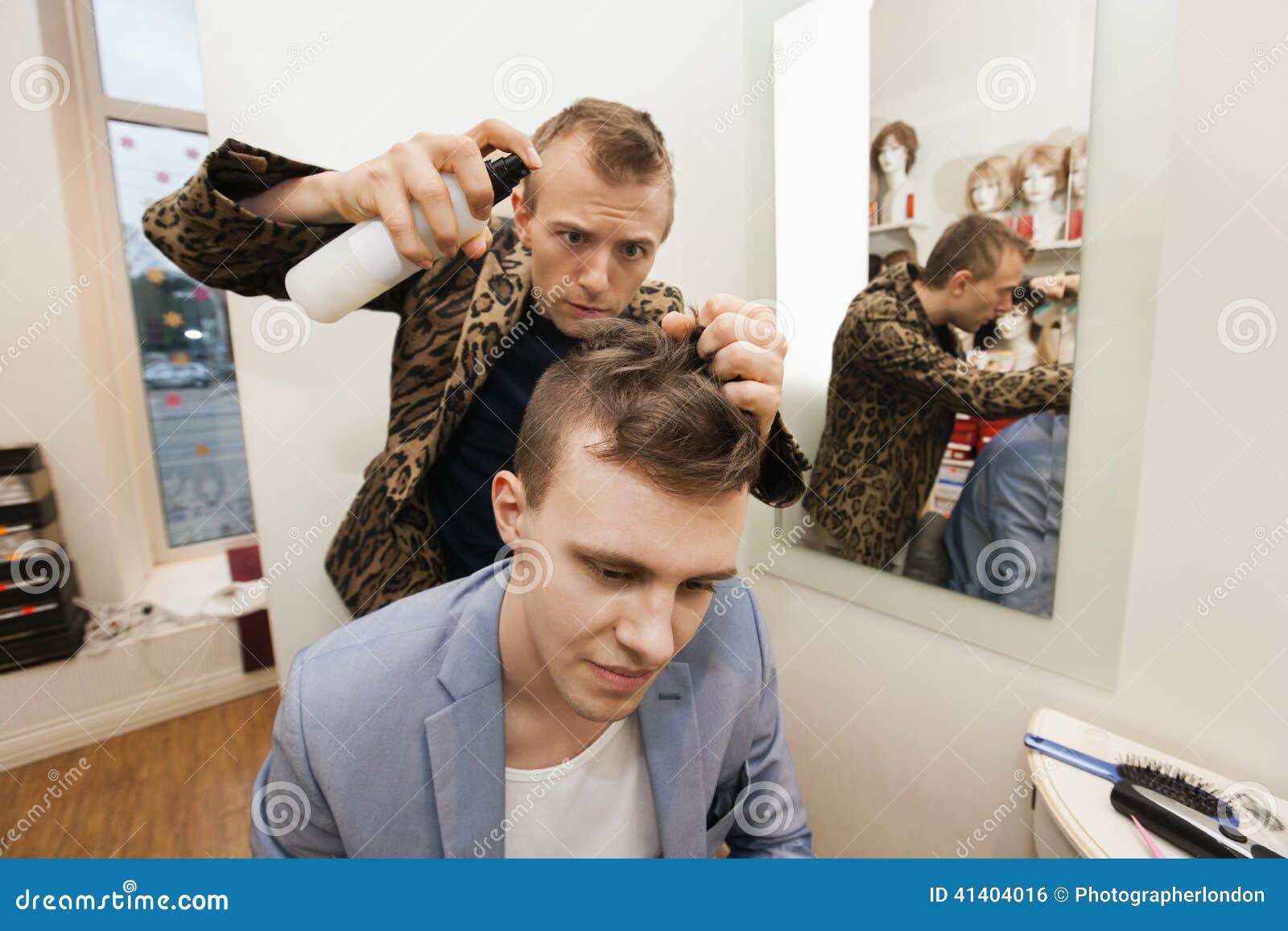 professional barber using hairspray on male customer in shop