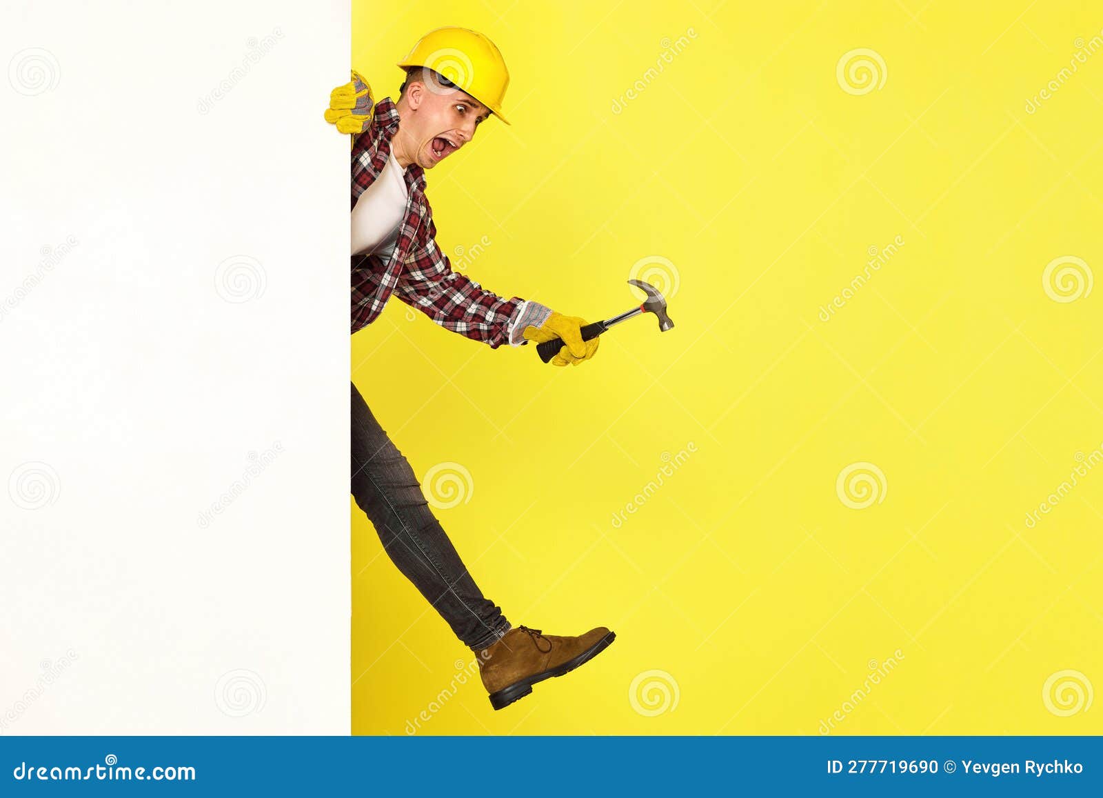 professional builder in work clothes in helmet holding hammer. professional builder in work clothes, helmet holds hammer and comes out from behind the banner. copy space for text