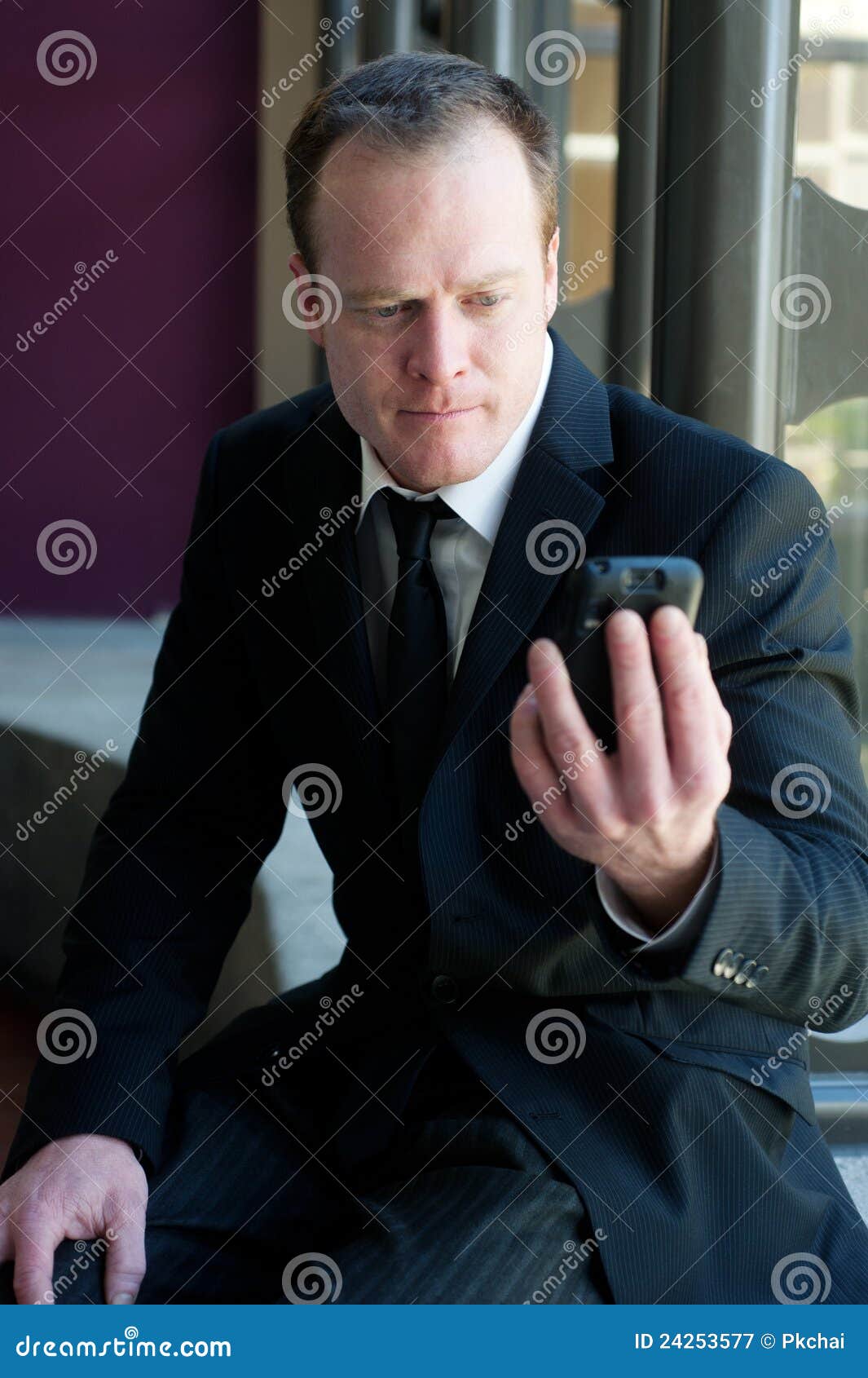 Professional businessman staring at cell phone sitting inside a building