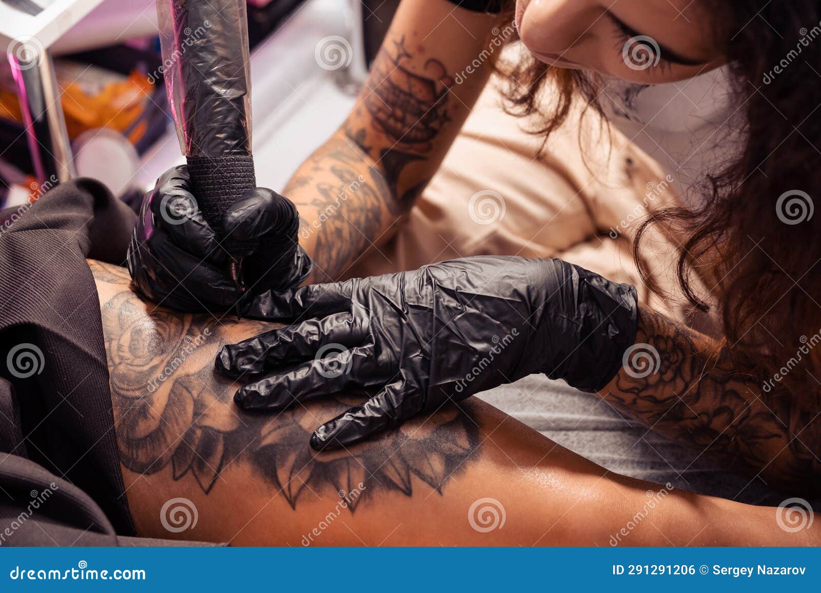 professional tattooist creating black and white flower  on female thigh